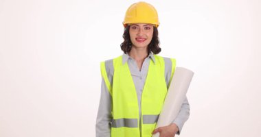 Sert şapkalı ve yüksek görüşlü yelekli bir kadın sarılı çizimler tutarken başparmak hareketi yapıyor. İnşaatçı inşaatla ilgili başarıyı ifade etti