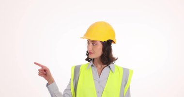 Sarı kasketli ve yüksek görüşlü yelek giyen, işaret parmağıyla yan yana duran bir kadın. Kadın mühendis belli bir noktaya dikkat çekiyor