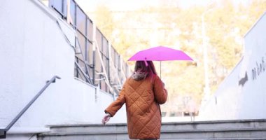 Kadın parlak pembe şemsiyeyi sıkıca tutuyor ve hızla merdivenlerden tırmanıyor. Şık giyinen bir kadın merdivenlerde hız kazanır. Yavaş çekim