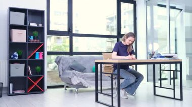 Sarışın kadın modern oturma odasındaki masada oturur ve günlük notlar ve planlar yazar. Kadın, farklı kalemlerle önemli görevlerin altını çiziyor