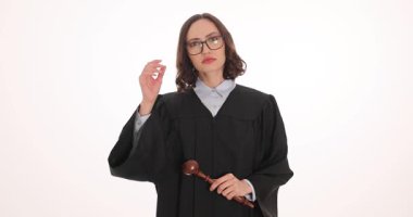 Kadın yargıç beyaz arka planda tokmak tutan gözlükleri çıkarır. Kendine güvenen siyah elbiseli kadın yargıç profesyonelliğini yavaş çekimde ifade ediyor.
