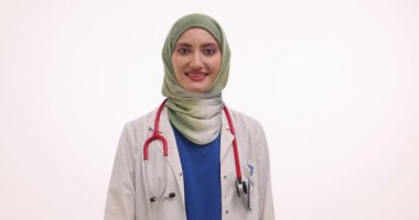 Tesettürlü genç kadın doktor beyaz arka planda iyi bir jest yapıyor. Müslüman kadın doktor yavaş çekimde tedavi planına onay ve destek verdi