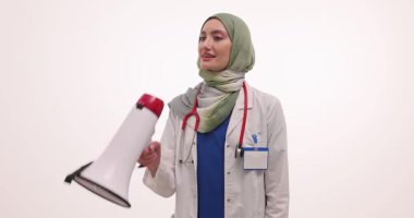 Tesettürlü kadın doktor megafonu dudaklarına kaldırır ve beyaz arka plana karşı konuşmaya başlar. Doktor önemli bir mesaj iletti. Yavaş çekim