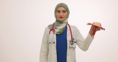 Türbanlı kadın jinekolog, beyaz arka planda rahmin anatomik modelini tutuyor. Doktor hasta için tavsiye edilen hapları gösteriyor. Yavaş çekim
