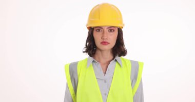 Güvenlik kaskı takan kadın mühendis, beyaz arka planda hoşlanmadığını göstererek başını sallıyor. Yansıtıcı yelek giyen kadın işçi, iş yerindeki anlaşmazlığını dile getirdi