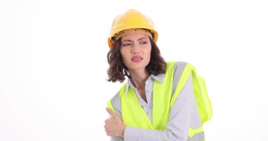 Çelik yelek giyen bir kadın beyaz duvarda acı verici bir masaj yapıyor. Miğferli kadın çalışan işyerinde yaralandığı için fiziksel olarak zorlanıyor.