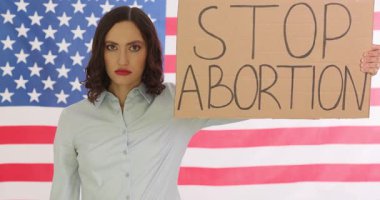 Kararlı kadın kürtajı Amerikan bayrağının pankartı ve el hareketiyle durdurmak istiyor. Sağ kanat eylemcisi Amerika 'da kürtaj karşıtı gösterilere katılıyor