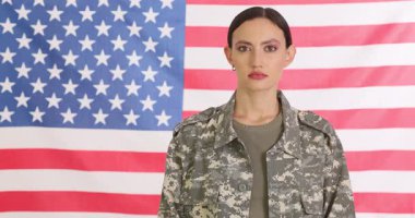 Askeri üniformalı bir kadın arka planda Amerikan bayrağıyla kollarını kavuşturuyor. Kendine güvenen genç bayan asker anavatanına ağır çekimde hizmet ediyor.