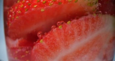 Beyaz arka planda köpüklü su bardağının içinde taze çilek dilimleri. Sıcak bir günde sulu böğürtlenli sağlıklı yaz kokteyli.