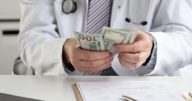 Paltolu ve steteskoplu doktor masada oturan dolarları sayıyor. Tıbbi belgeler sağlık giderleri ve mali açıdan