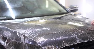 Koyu renkli araba kaputu şeffaf koruyucu filmle kaplı. Garajdaki başvuru sürecini gösteren uygulamalı film üzerindeki kabarcıklar ve kırışıklıklar
