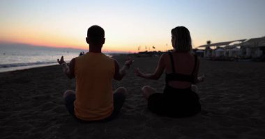 Sakin adam ve kadının siluetleri kumsalın arka penceresinde meditasyon yapıyor. Dikkatli çiftler gün batımında kıyıda nefes alma egzersizleri yapıyor.