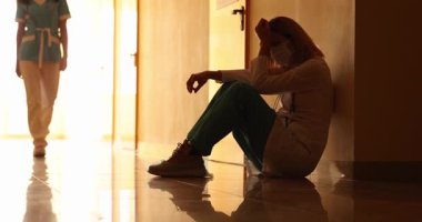 Yoksul kadın doktor hastane koridorunda yerde otururken ağlıyor. Hasta ölümünün etkisiyle kalbi kırık bir kadın doktor ve hemşire sağlık merkezinin önünden geçiyor.