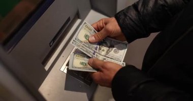 Adam geceleri sokakta ATM 'nin yanında duran dolarları sayıyor. Müşteri, açık havada otomatik bankacılık ekipmanlarıyla nakit para çekiyor.