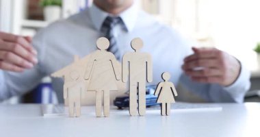 Sigorta acentesi oyuncak ahşap aileyi ve masasında koruyacak elleri olan arabayı karşılıyor. Yönetici, işyerinde meydana gelen kazalardan kaynaklanan finansal kapsama planını gerçekleştirir.