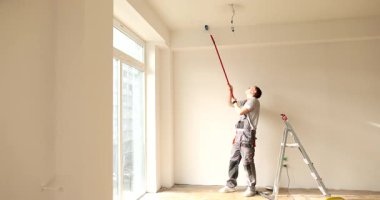 Ressam tavandaki en yüksek noktalara ulaşmak için kollarını uzatır. İnşaat işçisi düzensiz yamalardan kaçınmak için uzun saplı silindir kullanıyor. Yavaş çekim