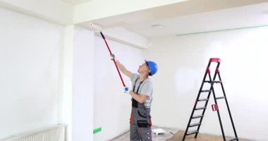 Zanaatkar, odanın tavanını beyaz boyayla boyamak için paten kullanır. İnşaat işçisi, pürüzsüz ve sabit vuruşlarla yeni boyalar sürüyor.