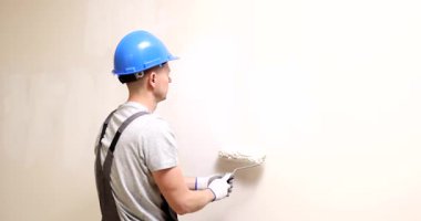 İnşaat işçisi beyaz boyayı oda duvarına eşit olarak uygulamak için paten kullanıyor. Deneyimli inşaatçı yüzeyde pürüzsüz bir son yaratır. Yavaş çekim