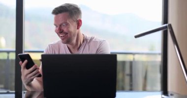 Heyecanlı adam akıllı telefon ekranına bakar ve büyük bir gülümsemeyle dizüstü bilgisayarı gösterir. Neşeli adam şaşırtıcı bir mesaj okuyor ve sevinçten yumruklarını kaldırıyor.