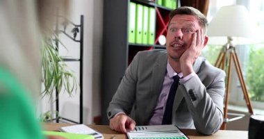 Takım elbiseli bir adam masanın karşısında oturmuş projeyi tartışıyor ve kağıtları gözden geçiriyor. Ofis çalışanları işyeri toplantısından sıkılmış ve ilgisiz görünüyorlar