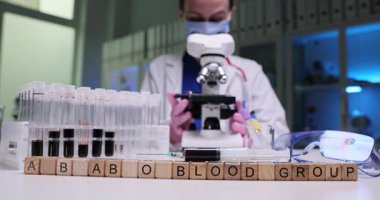 Kendini adamış bir bilim adamı, profesyonel bir laboratuvar ortamında mikroskopla titizlikle kan grubu analizi yapıyor.