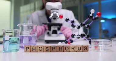 Bir bilim adamı mikroskop altında renkli çözümler ve gözlemlerde moleküler modeller kullanarak fosfor üzerinde çalışır.
