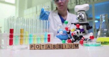 Bir bilim adamı potasyum üzerinde test tüpleri, moleküler modeller ve modern bir laboratuvar ortamında mikroskop kullanarak çalışır.