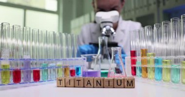 Canlı bir bilimsel araştırma ortamında renkli test tüpleri ve titanyum materyalleri gösteren bir laboratuvar sahnesi.