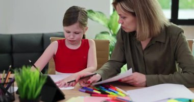 Anne ve kızı tablet ve renkli kalemlerle masada oturuyorlar. Kaliteli zamanlarda yaratıcılığı çizerken ve beslerken neşeli anlar