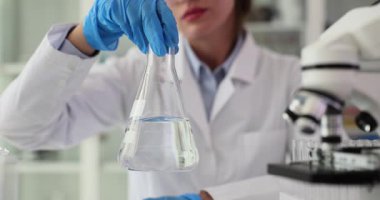 Koruyucu ekipman araştırmacısı, steril laboratuvar ortamında mikroskop ile cam matarayı temiz sıvı bilimsel araştırmalarla idare ediyor.