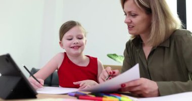 Anne, masada tablet kullanarak kızına ev ödevlerinde yardım ediyor. Çevrimiçi öğrenim teşvik eğitimi ve evde aile bağı