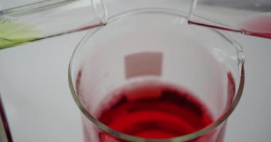 Test tüplerinden deney tüplerine sarı ve kırmızı kimyasal sıvılar dökülüyor. Laboratuvarda reaksiyonu incelemek için farklı renk maddeleri karıştırılıyor