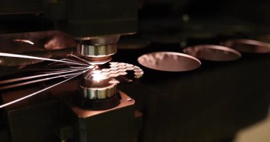 Endüstriyel lazer kesme makinesi karanlıkta atölyedeki metal parçalarını işliyor. Makine, modern fabrikada hassasiyet gösteren kıvılcımlar üretir.