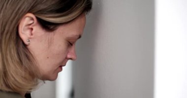 Çaresiz kadın alnını yavaşça soğuk duvara yaslıyor. Hayal kırıklığına uğramış sarışın kadın yüzü derin bir üzüntü ve yorgunluk belirtileri gösterir.