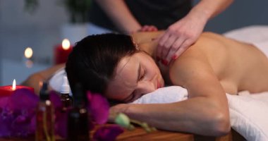 Terapist, bayan müşterinin yastıklı masada dinlenmesi üzerine masaj yapıyor. Çıplak sırtlı mutlu genç bir kadın güzellik salonunda spa prosedürlerini sever.