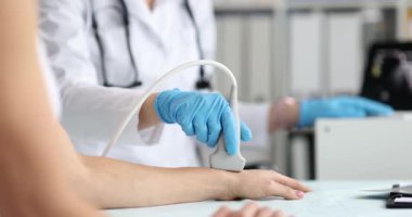 Mavi eldivenli doktor, klinikte hasta bileğini ultrasonla muayene ediyor. Doktor, tıp merkezinde tanı görüntüleme için dönüştürücü kullanır.