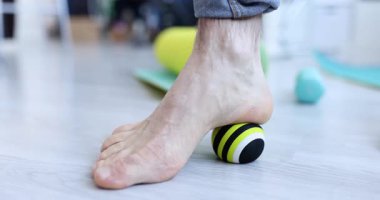 Adam ayak kemerine evde yerde küçük bir topla masaj yapıyor. Hasta, plantar fasiitis ağrısını dindirmek için kendine yardım ediyor. Spor salonunda rahatlamayı teşvik ediyor.