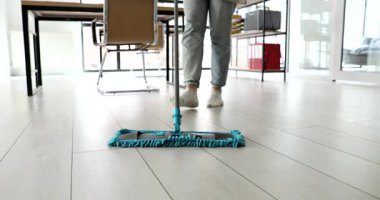 Temizlikçi modern ofiste mikrofiber paspas kullanarak ahşap yerleri dikkatlice paspaslar. Ev hanımı tozları silmek ve tertemiz bir görünüm sağlamak için paspas kullanıyor.