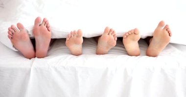Aile üyeleri yataktaki beyaz battaniyenin altından çıplak ayakla çıkar. Yatak odasında rahat ve rahat bir sabah geçirmenin sıcaklığı ve birlikteliği.
