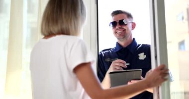 Polis memuru kapıdaki kadınla konuşurken tablete yazıyor. Mahalle güvenliği ve toplum güdümlü yasa uygulama etkileşimi