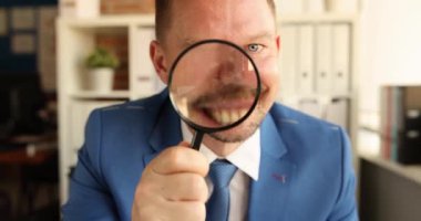 Ofisteki büyüteçten bakan neşeli işadamı gülümsüyor. Girişimci, işyerinde kalkınma için iş fırsatları arıyor