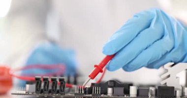 Eldivenli teknisyen devre kartındaki kırmızı çoklu metre sondasını inceliyor. Teknik laboratuvar ortamında tanısal test