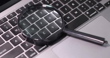 Laptop klavyesine yerleştirilmiş büyüteç tuşlara odaklanıyor. Olay yeri, iş yerinde online araştırma veri analizi ve siber güvenlik araştırması yapılmasını öneriyor
