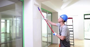 Kasklı bir ressam, apartman tadilatı sırasında duvarlara beyaz boya sürüyor. İşçi, iç mekanı muhafaza eden modern ofisi yeniden dekore ediyor.