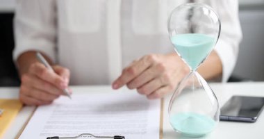 İş kadını önemli yasal belgeleri imzalarken kum saati görev süresini ölçüyor. Zaman yönetimi kavramları ve teslim tarihinin baskısı