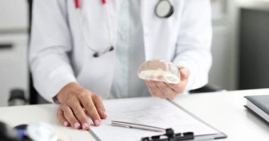 Doktor ellerinde silikon göğüs implantı var. Klinikteki hastaya durumu açıklıyor. Estetik cerrahi konusunda kadın tıp uzmanları danışmanlık yapıyor.