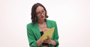 Gözlüklü genç iş kadını sarı not defterine notlar yazıyor. Pozitif kadın, beyaz arka planda ağır çekimde duran iş sezgilerini işaretliyor