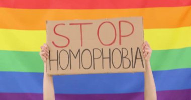 Büyük LGBT gökkuşağı bayrağına karşı üzerinde STOP HOMOPHOBIA mesajı olan mukavva tabelaları ellerde. Protestocu protesto etkinliği sırasında homofobiye son çağrısında bulundu