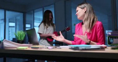 Genç stresli iş kadını gece evde çalışıyor ve gürültücü kızıyla ukulele oynarken tartışıyor. Bayan masadaki bilgisayara konsantre olmaya çalışıyor.