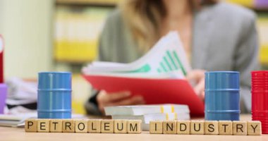 Kadın yönetici, Petrol Endüstrisi ile ahşap küplerle ilgili mali raporları analiz ediyor. Ofisteki masada duran mavi varillerin yanındaki grafikleri inceleyen kadın.